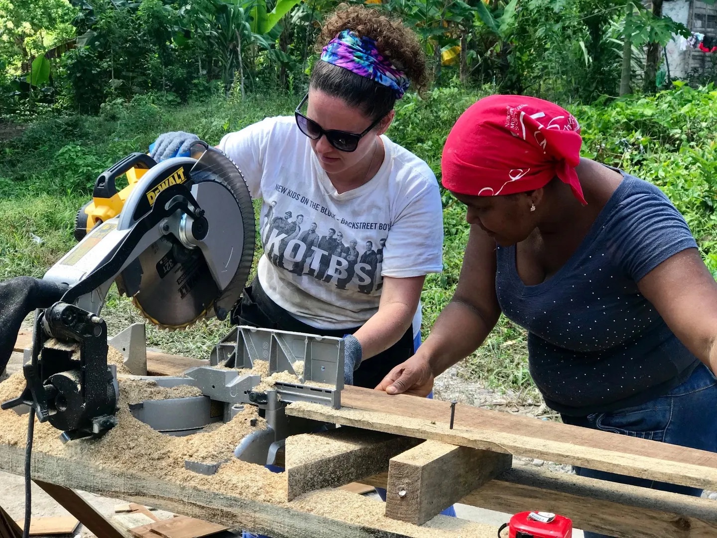 Volunteer using a saw alongside a local woman to cut lumber for construction