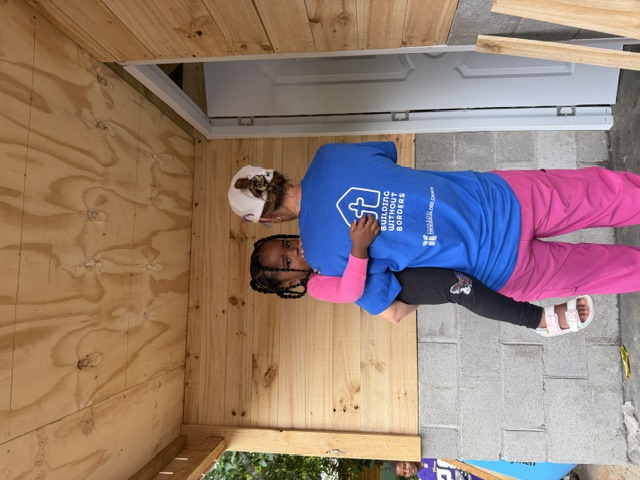 Volunteer holding a child on the porch of a newly built home