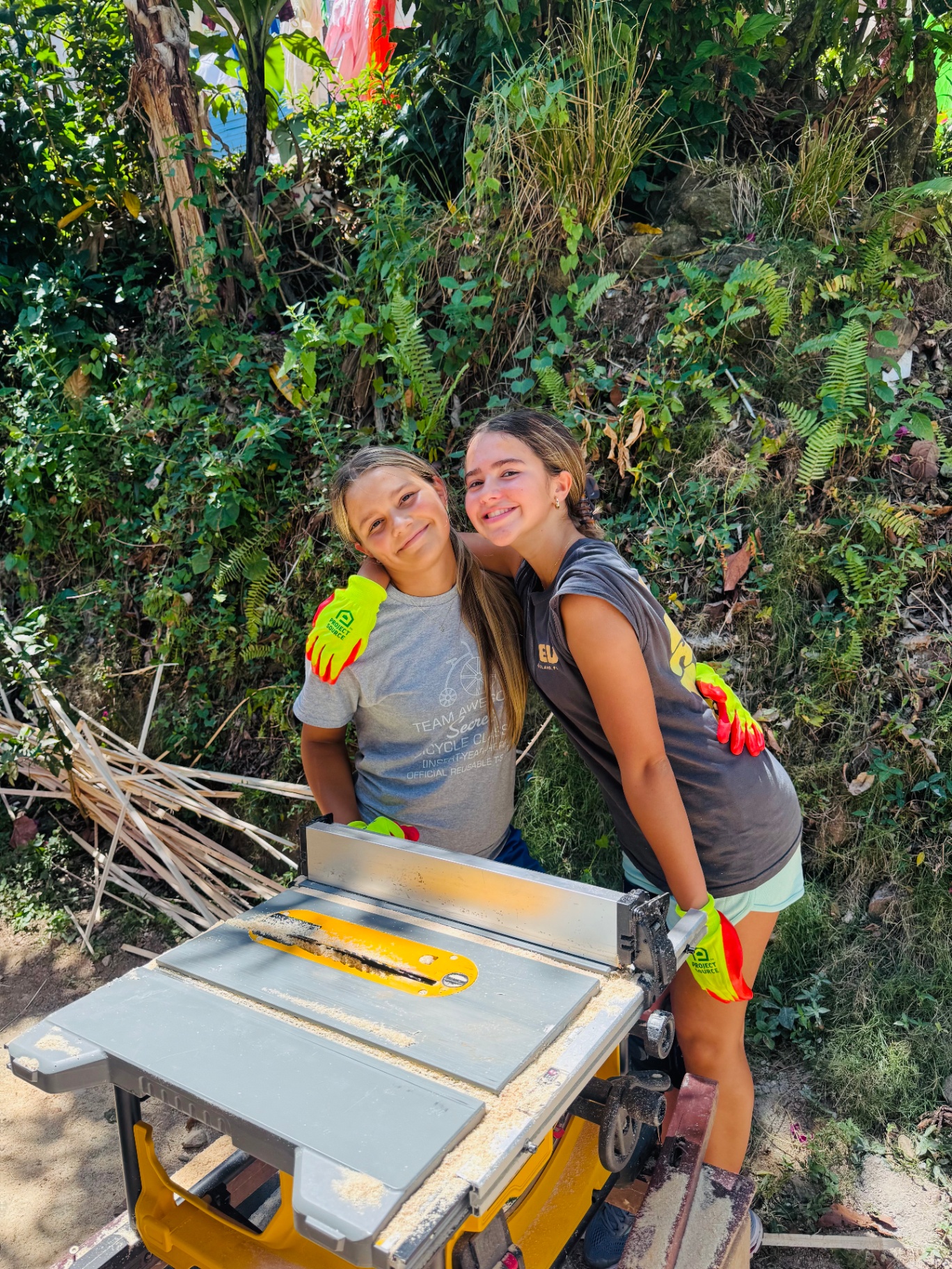 Two young volunteers smiling together by a table saw
