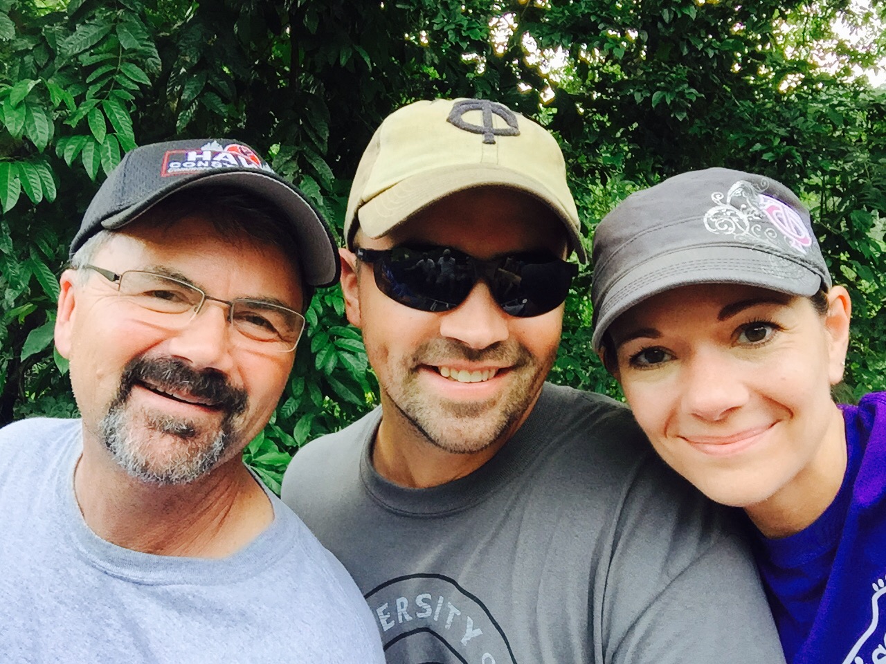 Three smiling volunteers taking a selfie in front of lush greenery