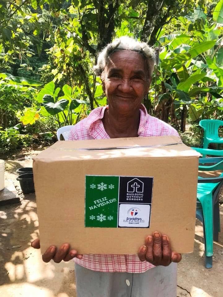 Smiling elderly woman holding a 'Feliz Navidad' food box delivery