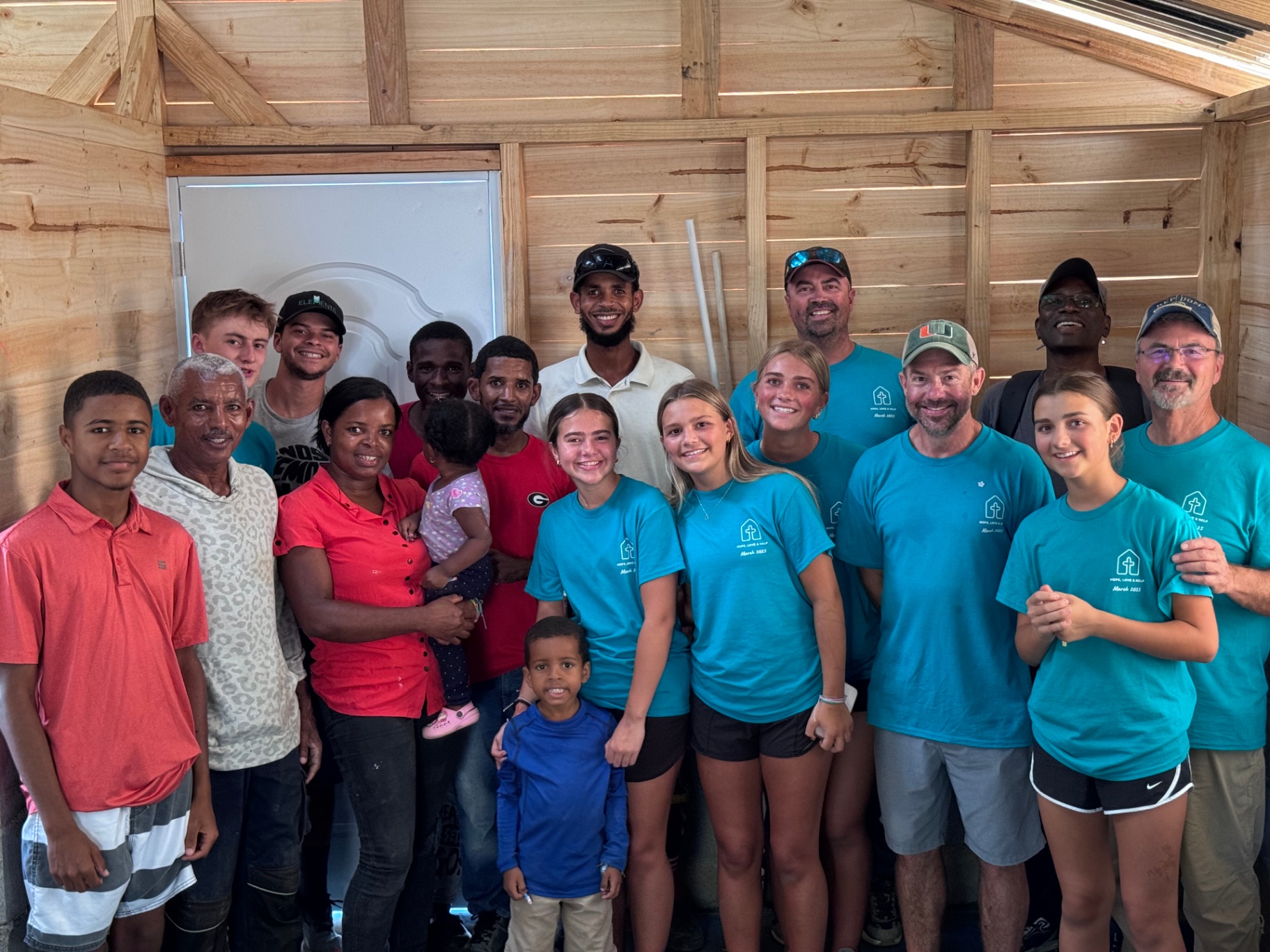 Large group photo of volunteers and local families inside a finished home