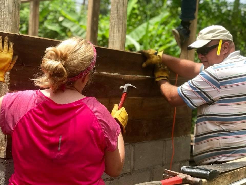 Two volunteers hammering wood siding onto a home under construction